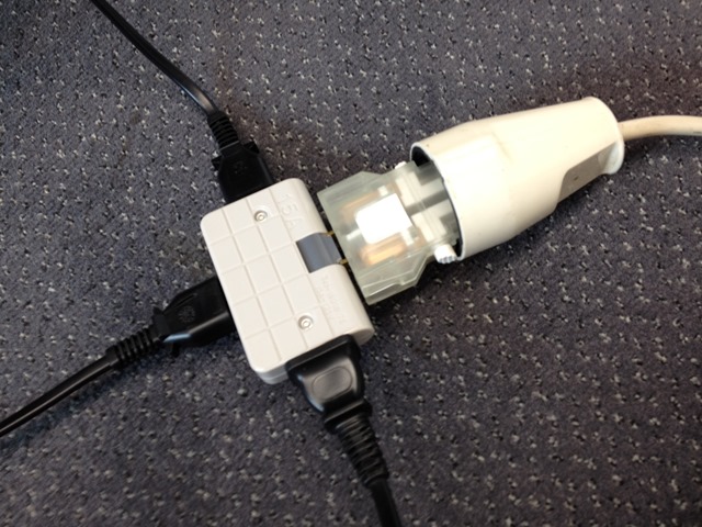 Close-up of an electrical plug adapter and cables resting on a carpeted floor, neutral grey and beige colors, calm technical mood